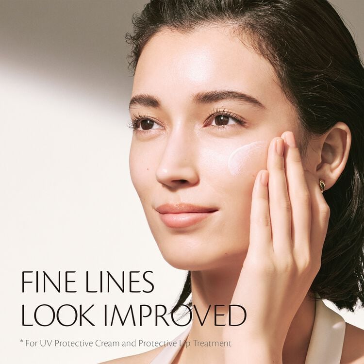 A young woman with brown hair applying UV Protective Cream to her cheek, showing improved fine lines.