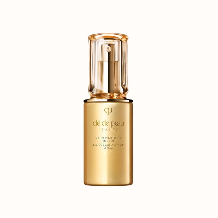 A gold-colored bottle of Clé de Peau Beauté Precious Gold Vitality Serum with a clear cap, isolated on a white background.