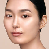 Close-up of a woman with her hair pulled back, featuring luminous skin and a small mole on her left cheek.