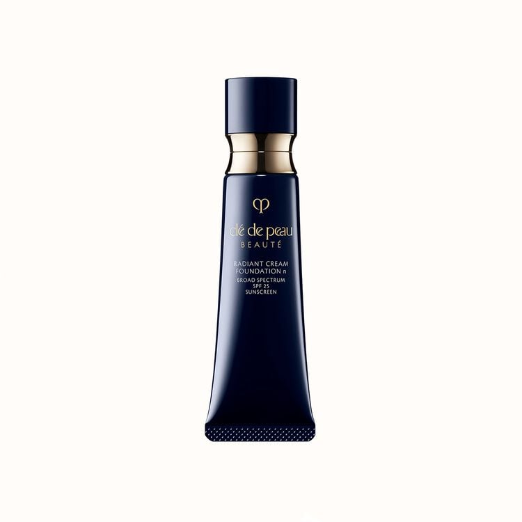 A slender, dark cosmetic tube of Radiant Cream Foundation SPF 25 standing upright with a metallic gold band near the top.
